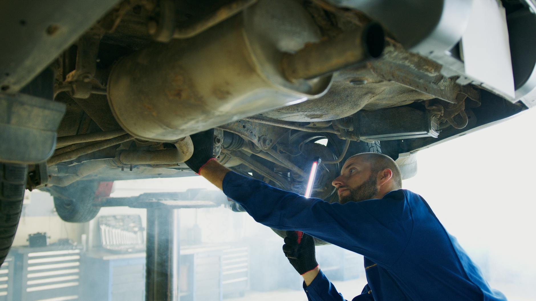 Mechanik diagnozuje układ wydechowy pod samochodem w warsztacie