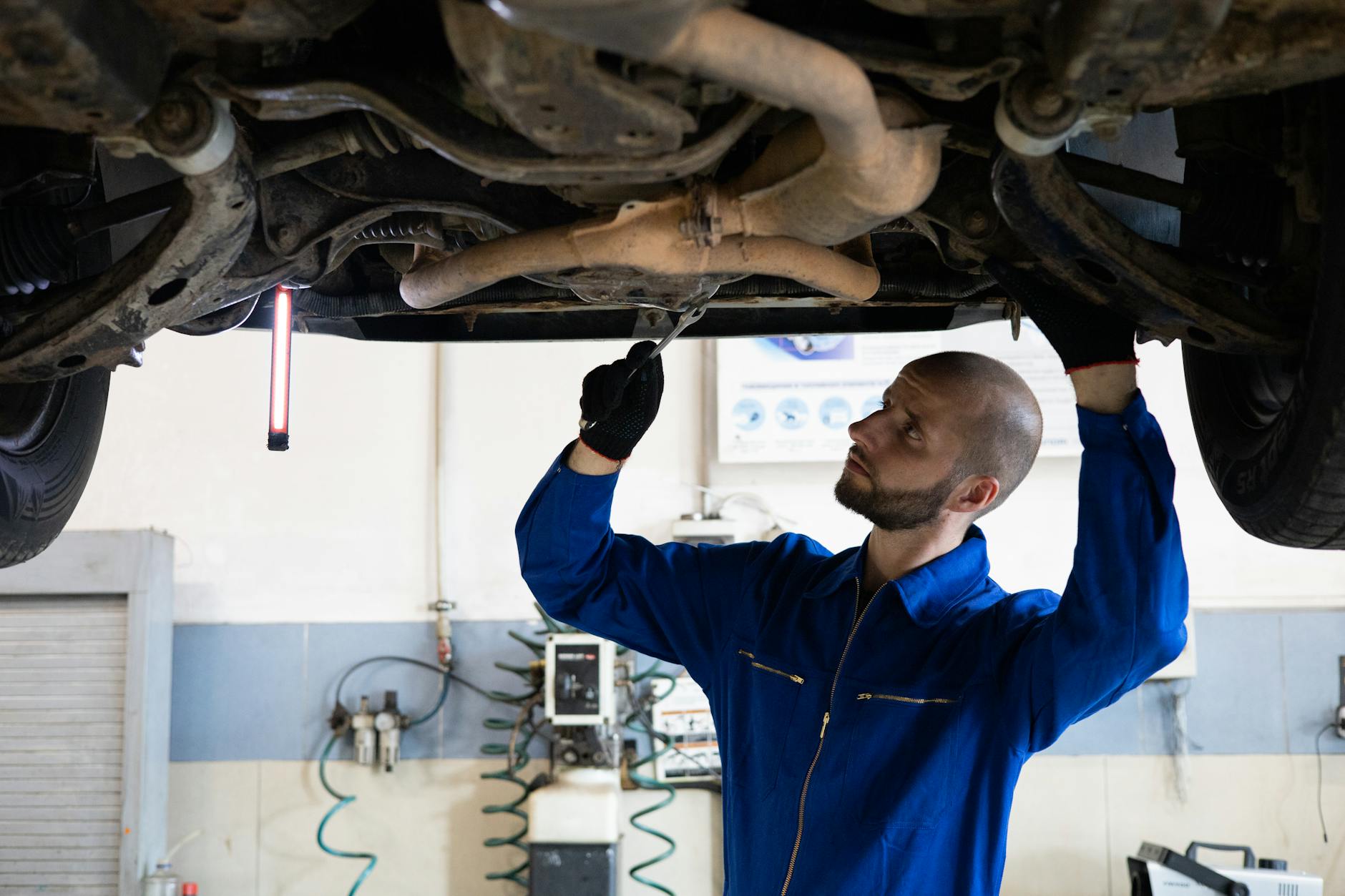 Mechanik w niebieskim kombinezonie ogląda układ wydechowy auta w warsztacie