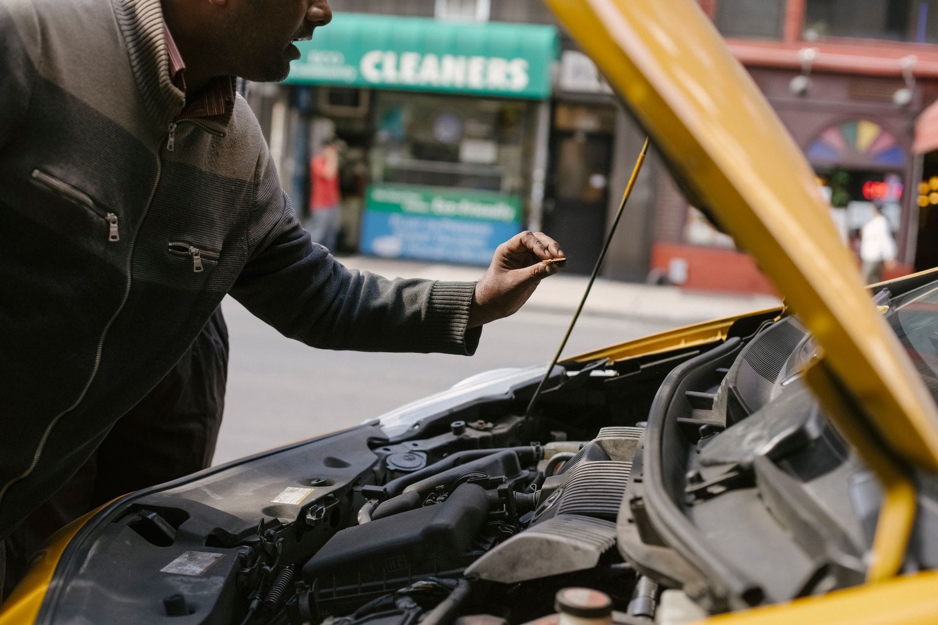 Mechanik pochylony nad silnikiem zepsutego auta na ulicy miasta Mechanik pochylony nad silnikiem zepsutego auta na ulicy miasta
