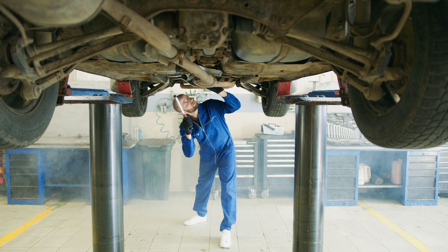 Mechanik w niebieskim kombinezonie ogląda auto na podnośniku w warsztacie