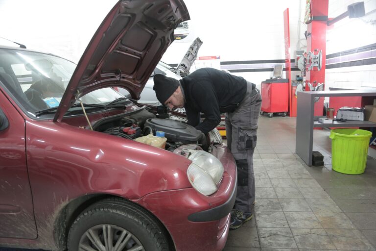Mechanik sprawdza silnik czerwonego samochodu w warsztacie